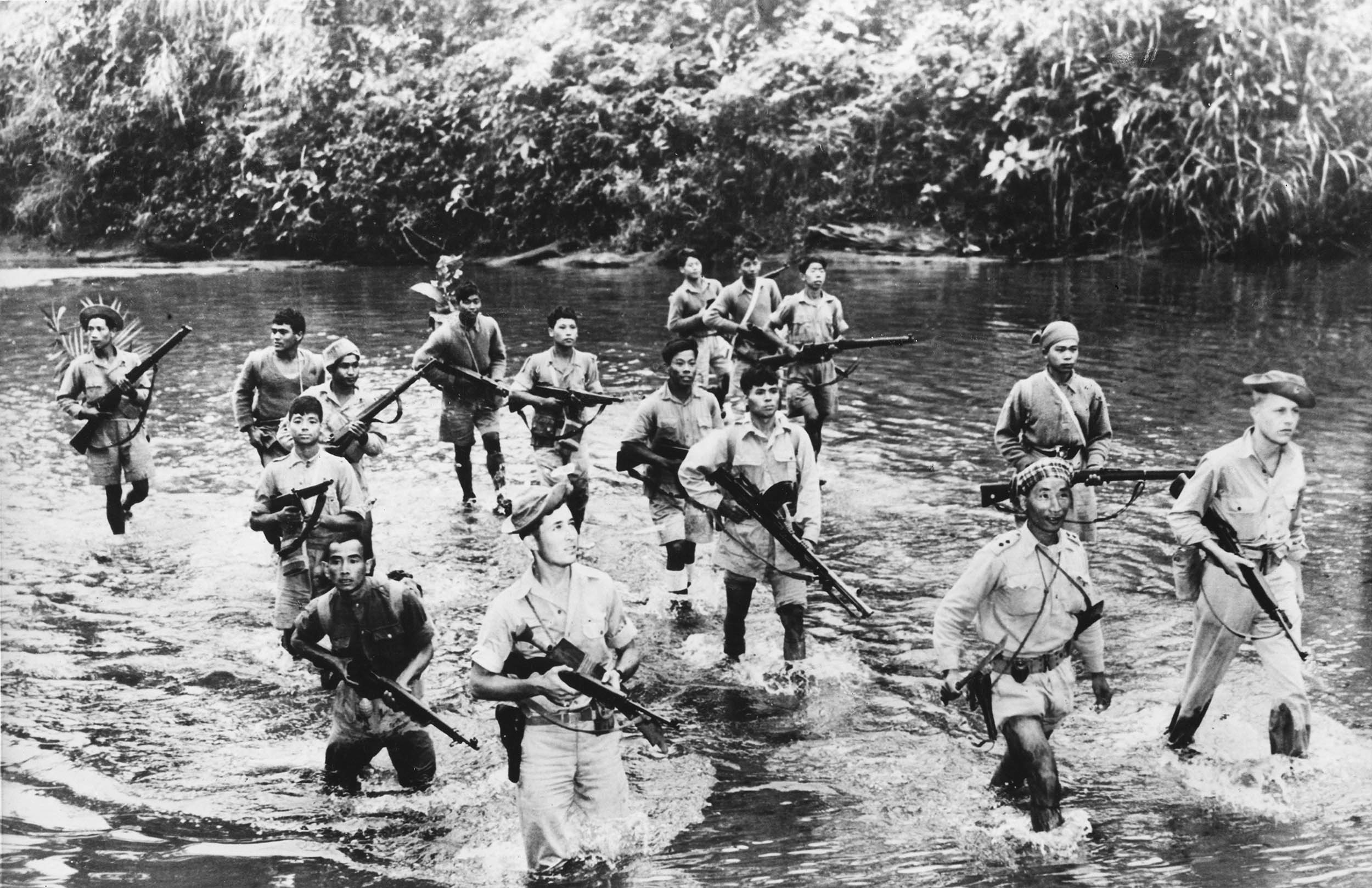 Scouting detachment of armed Burmese patriot fighters, accompanied by two American Soldiers, cautiously wades through jungle stream in Northern Burma, circa 1944 (Chronicle/Alamy)