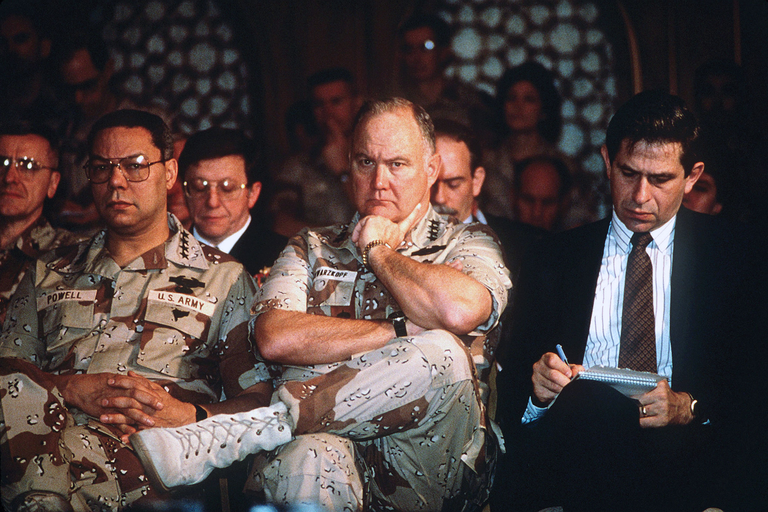 Paul D. Wolfowitz, Under Secretary of Defense for Policy, right, takes notes while General Colin Powell, Chairman of the Joint Chiefs of Staff; and General Norman Schwarzkopf, Commander-in-Chief, U.S. Central Command, take part in press conference held by U.S. and Saudi Arabian officials during Operation Desert Storm, circa February 1991