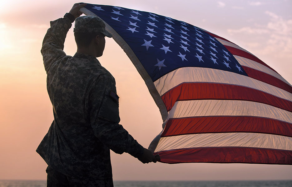 Soldier with Joint Forces Command–United Assistance, assigned to Headquarters and Headquarters Battalion, 101st Airborne Division (Air Assault), holds up U.S. flag during promotion and reenlistment ceremony, January 1, 2015, at Barclay Training Center, Monrovia, Liberia (U.S. Army/Rashene Mincy)