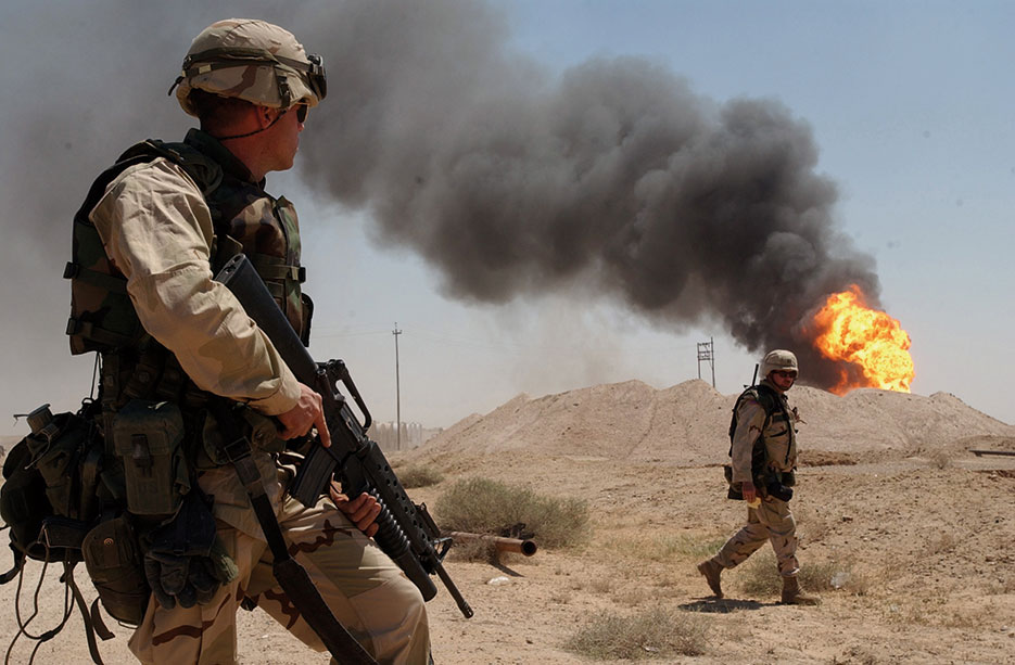 Soldier stands guard duty near burning oil well in Rumaylah Oil Fields in Southern Iraq, April 2003 (U.S. Navy/Arlo K. Abrahamson)