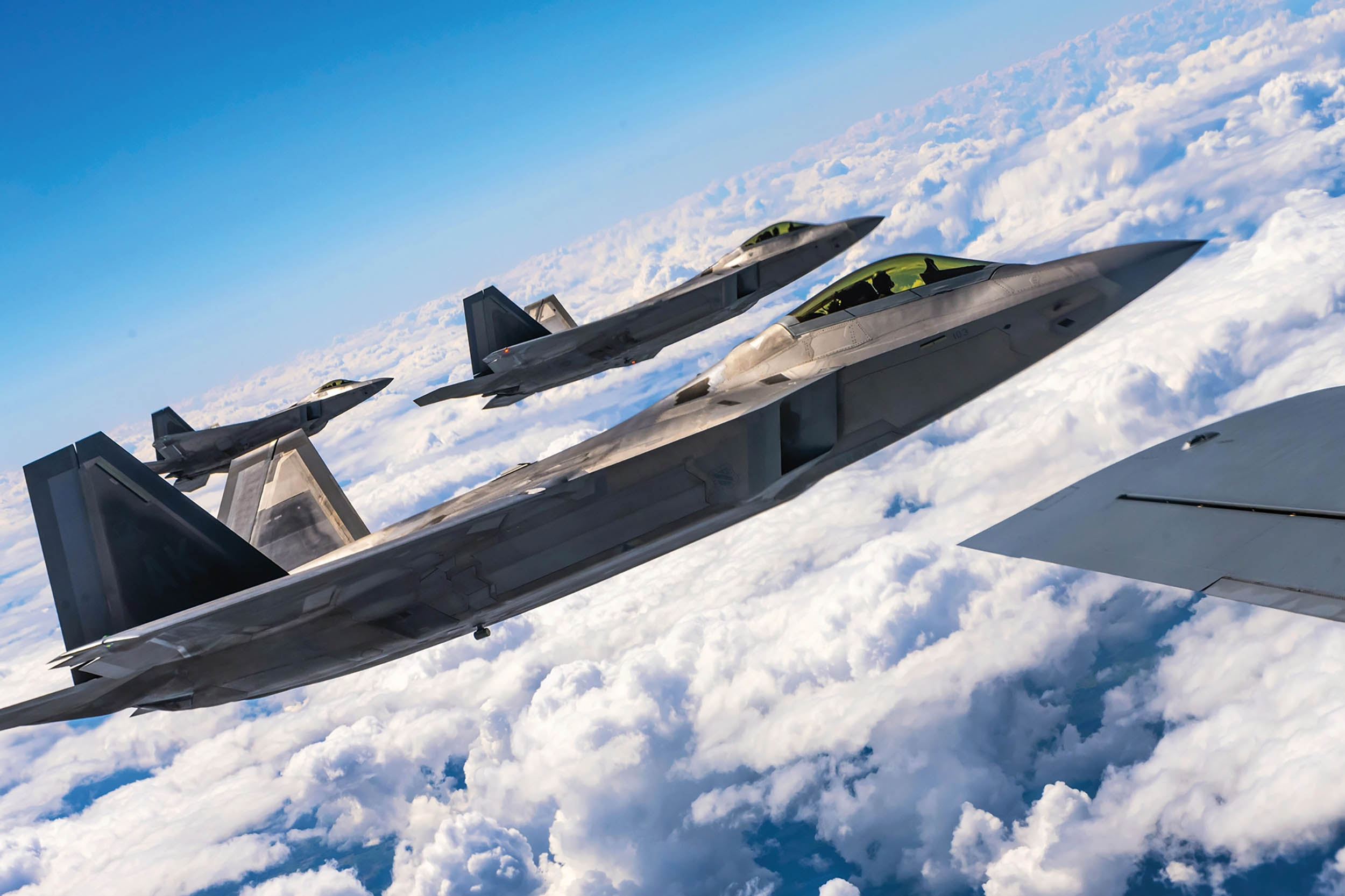 Three Air Force F-22 Raptor aircraft fly alongside Air Force KC-135 Stratotanker aircraft over Poland