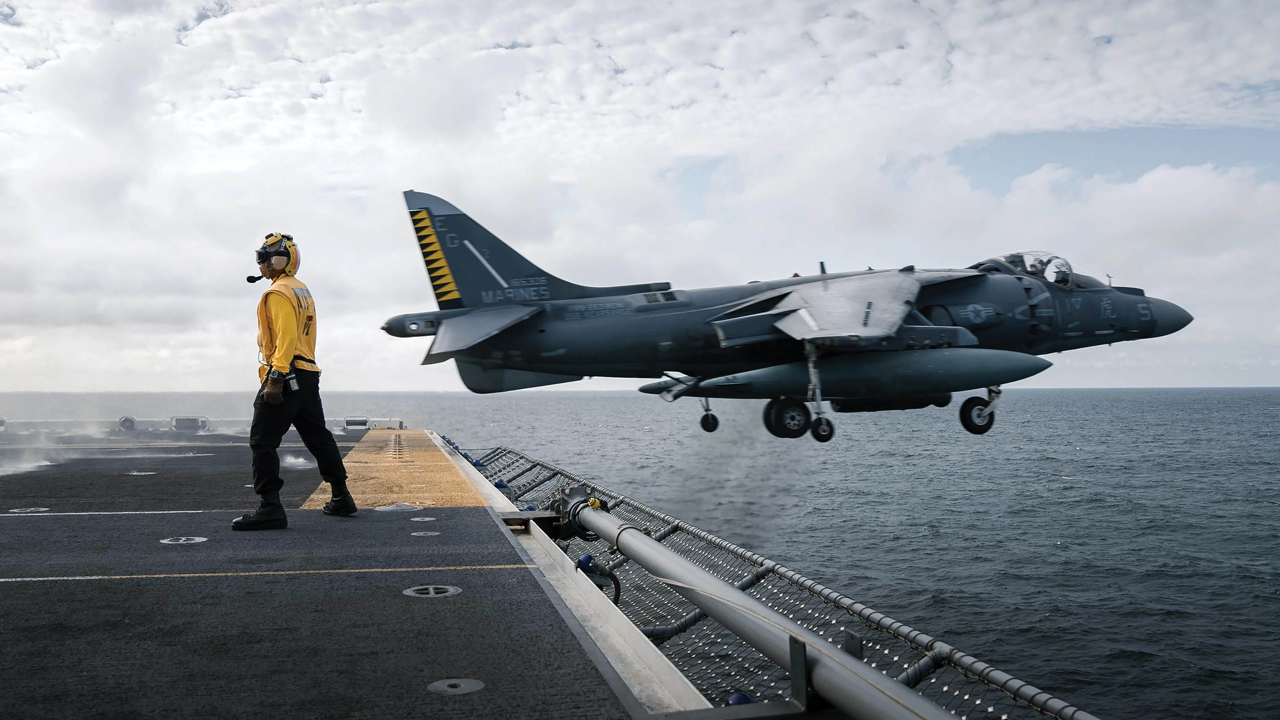 Marine Corps AV-8B Harrier attached to 22nd Marine Expeditionary Unit flies past Navy Aviation Boatswain’s Mate (Handler) 1st Class Tu N. Chau during flight operations aboard USS Kearsarge in Baltic Sea, August 24, 2022 (U.S. Navy/Taylor Parker)