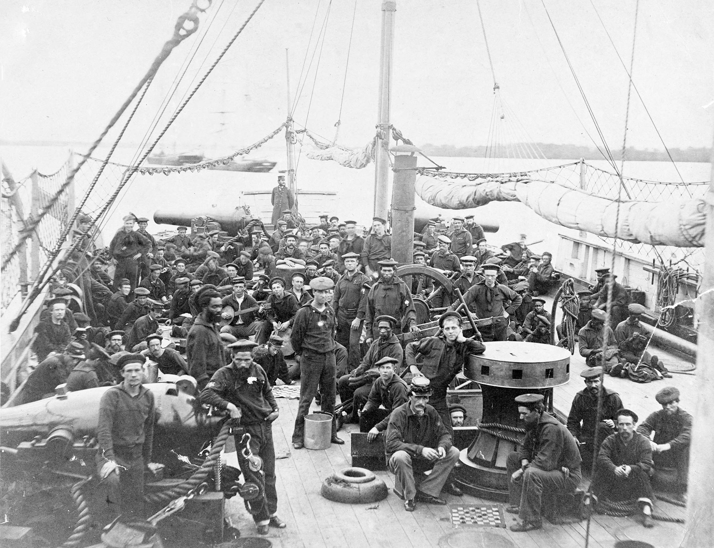 Members of USS Miami crew on forecastle, ca. 1864–1865; Frank W. Hackett, former officer of the ship, wrote in 1910: “The officer standing in the background, at the extreme prow of the ship, is W.N. Wells, Executive Officer. The man in the foreground with his arm on the nine-inch gun is White, the gunner. Sergeant of Marines, Stanley, is sitting in the foreground, near the capstan” (Naval History and Heritage Command)
